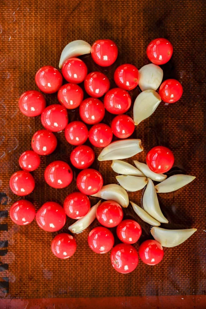 tomatos and garlic cloves on lined baking sheet before roasting