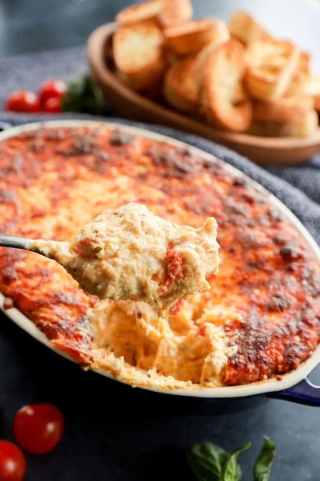 spoon lifting out four cheese baked appetizer from baking dish