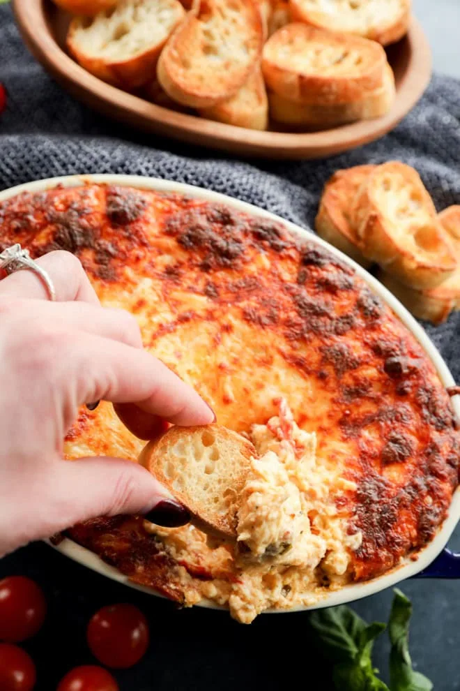 hand holding crostini to dunk into a baking dish of four cheese