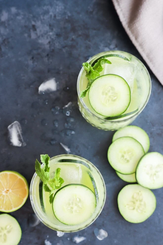 Overhead cucumber margaritas glasses with fresh vegetables and lime half