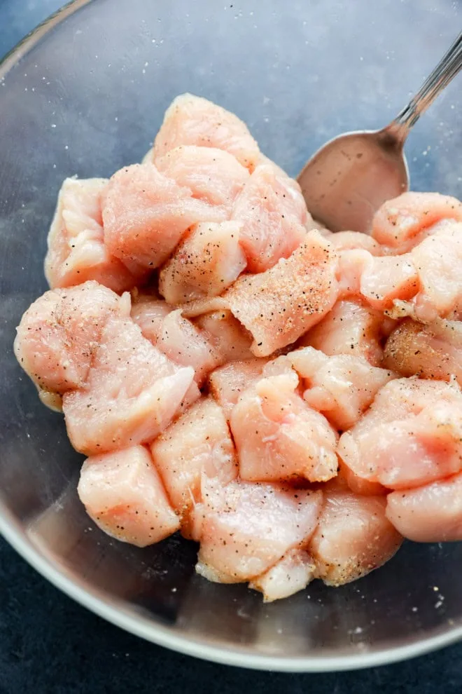 cubed chicken in a glass bowl with seasoning and spoon