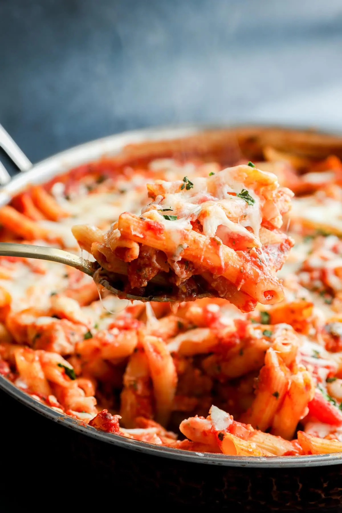 spoon lifting out italian penne dish with poultry and marinara sauce and cheese