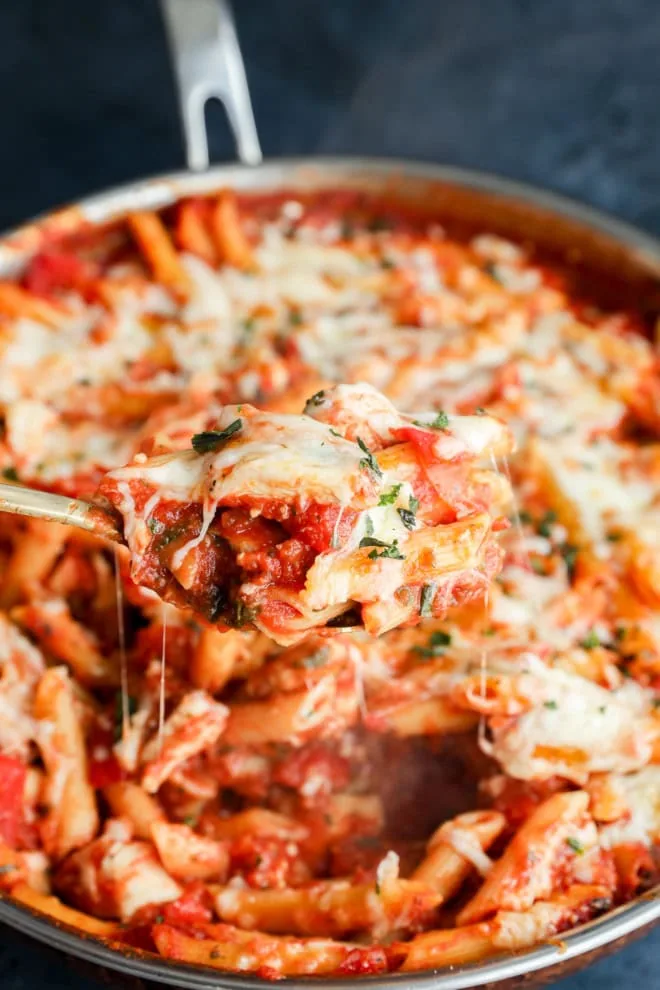 spoon lifting out gooey chicken parmesan pasta from the skillet