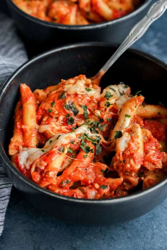 a bowl of chicken parmesan pasta with a spoon and fresh basil on top