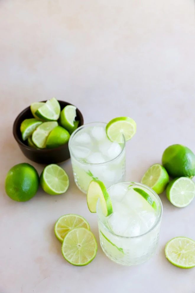 glasses of caipirinha with a bowl of fresh lime wedges and whole limes in the background