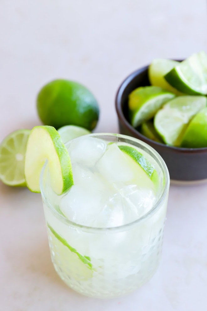 caipirinha in a glass garnished with limes and a bowl of limes in the background