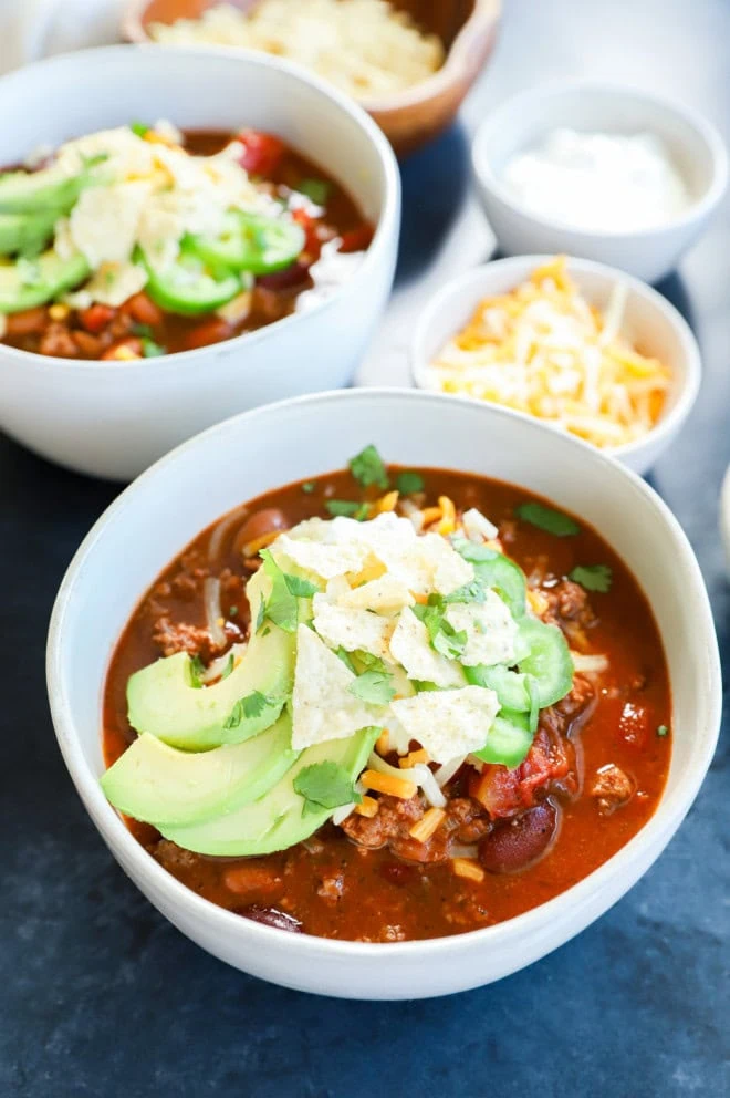 Bowls of spicy taco chili with toppings and cheese in a small bowl