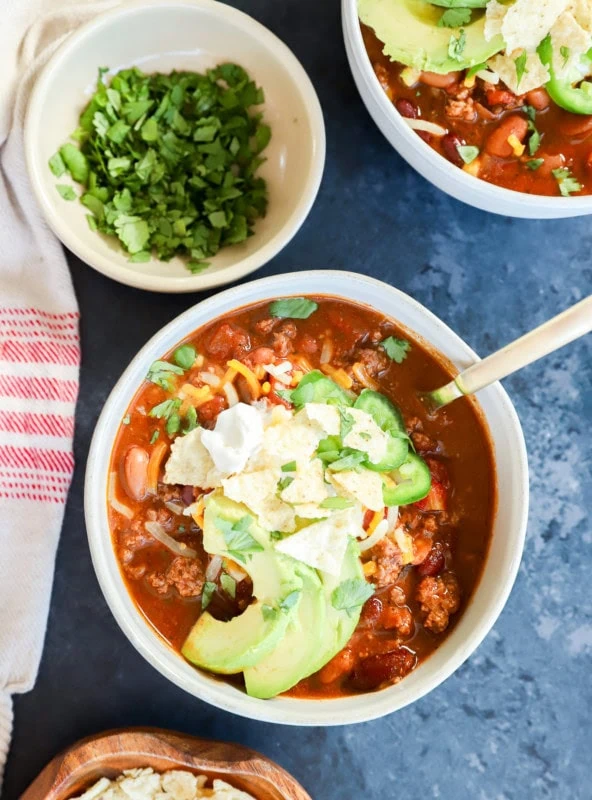 Bowls of taco soup with spoons and bowls with toppings