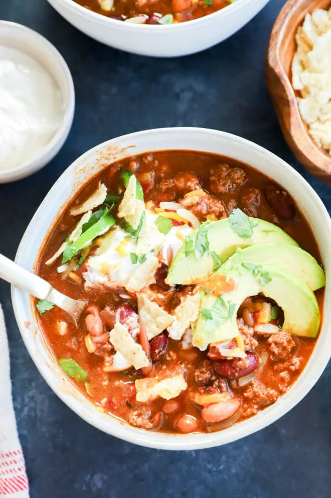 A bowl of spicy soup with a spoon with toppings