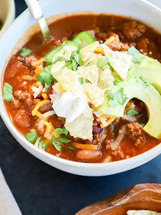 Spicy taco chili in a bowl with avocado, sour cream, and cheese