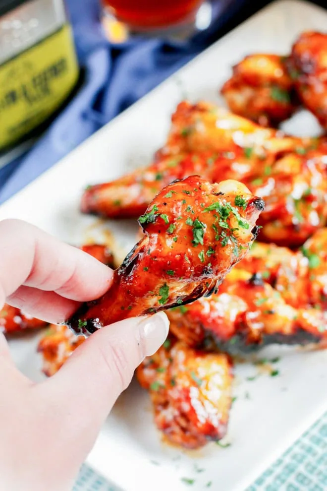 hand holding a chicken wing with BBQ sauce and spices in the background