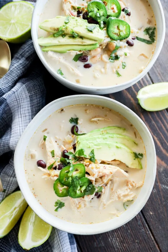 two bowls of soup with lots of toppings and lime wedges on the side