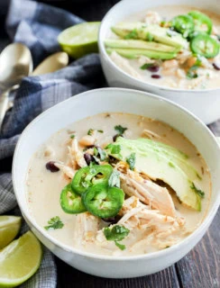 Slow cooker creamy white chicken chili in bowls with toppings and limes