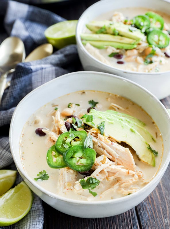 Slow cooker creamy white chicken chili in bowls with toppings and limes