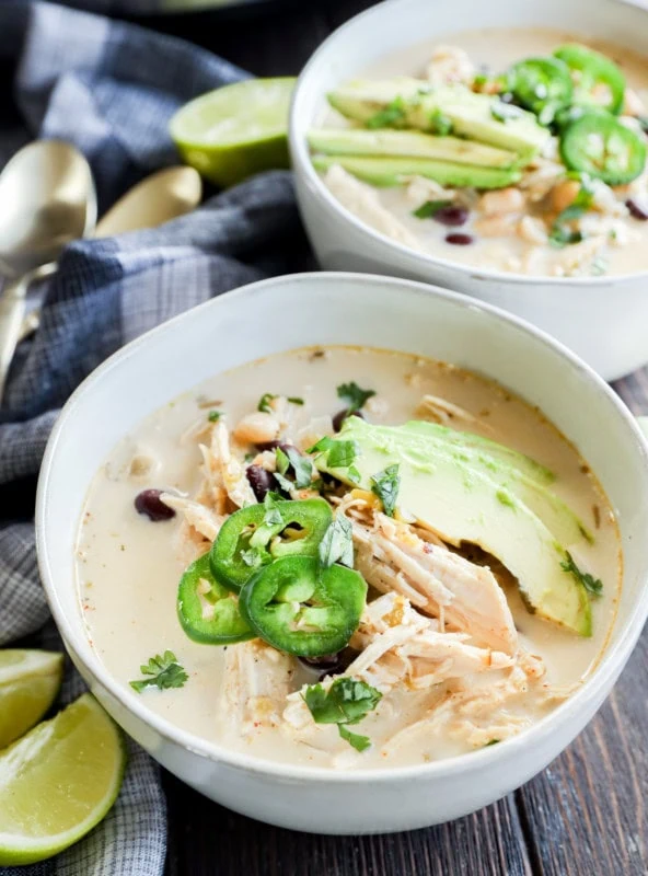 Slow cooker creamy white chicken chili in bowls with toppings and limes