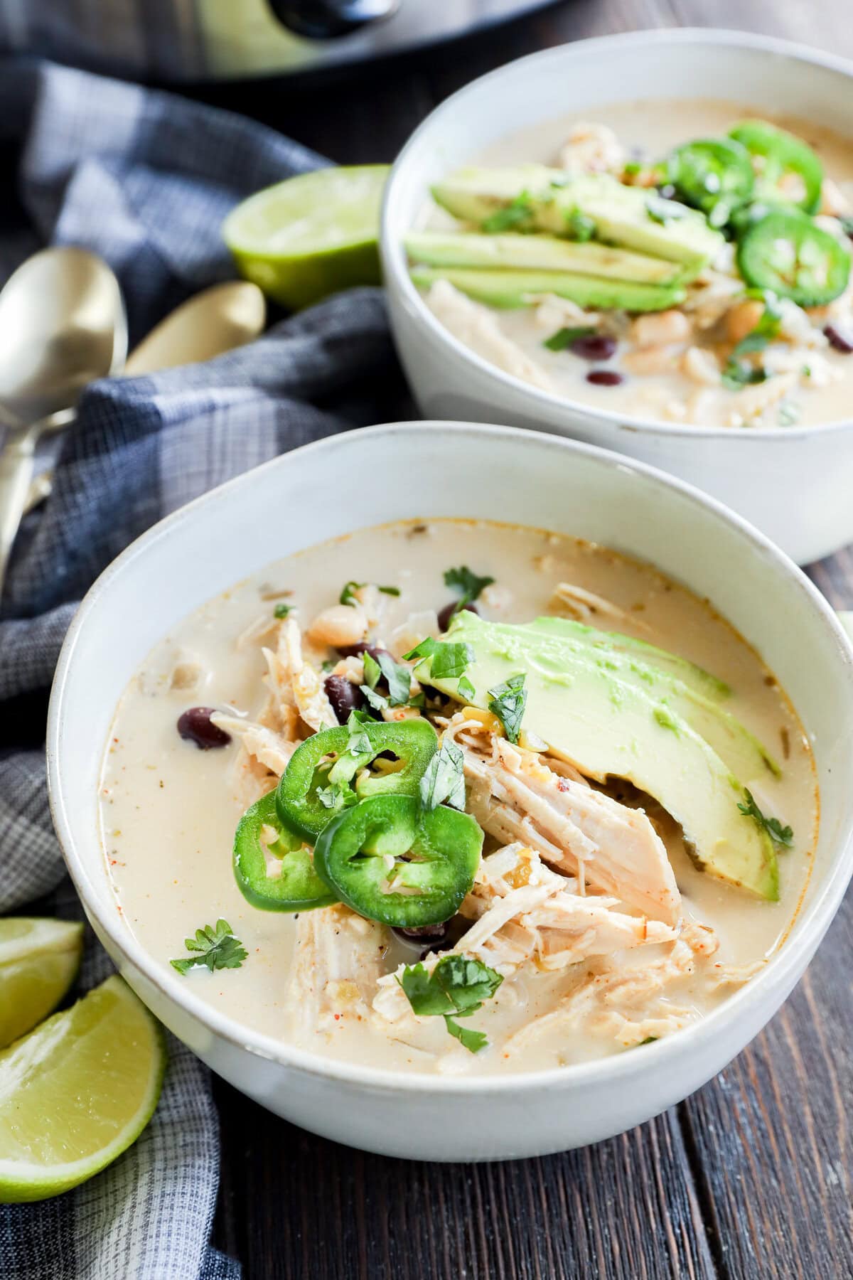 Slow cooker creamy white chicken chili in bowls with toppings and limes