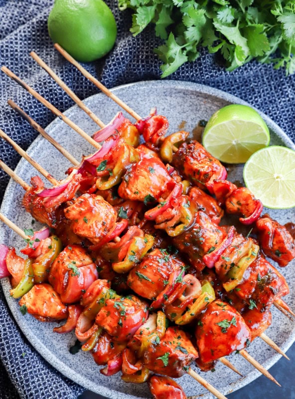 Plate of grilled bbq chicken kabobs with lime halves and cilantro bunch