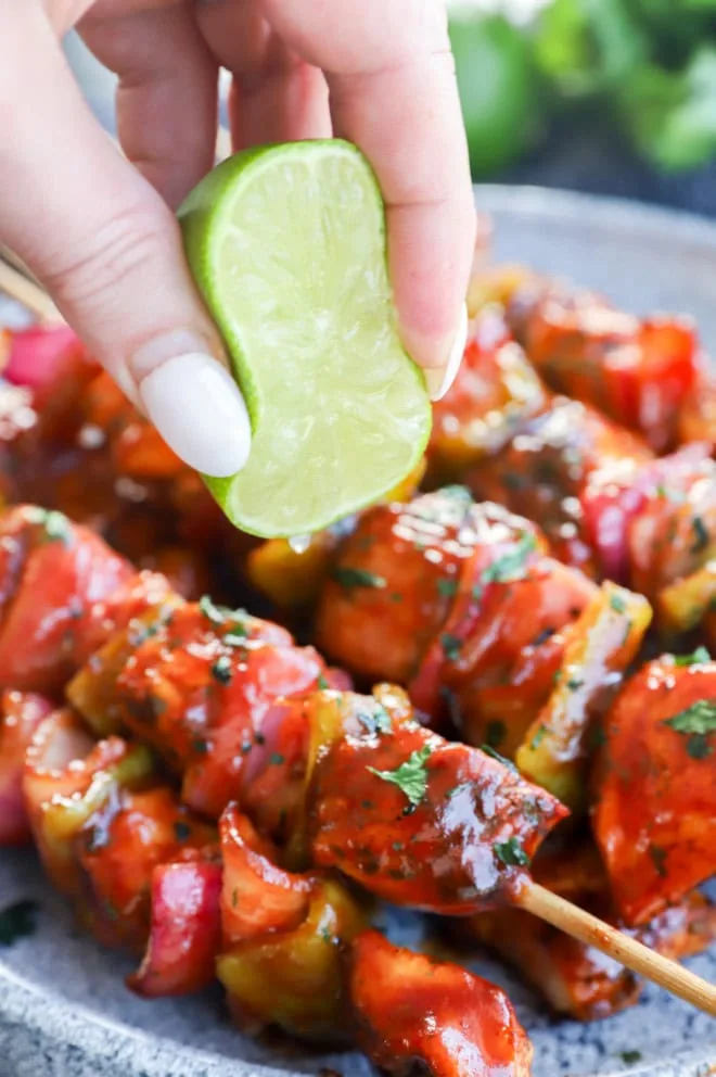 Hand squeezing lime over barbecue poultry and vegetables