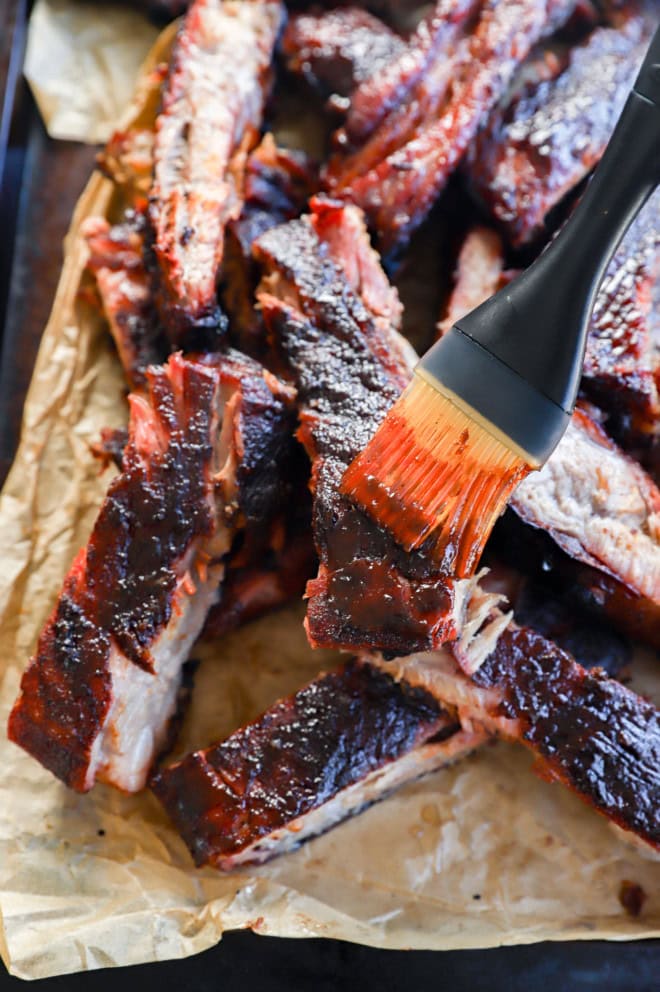 brushing bbq sauce on pork sliced on parchment paper