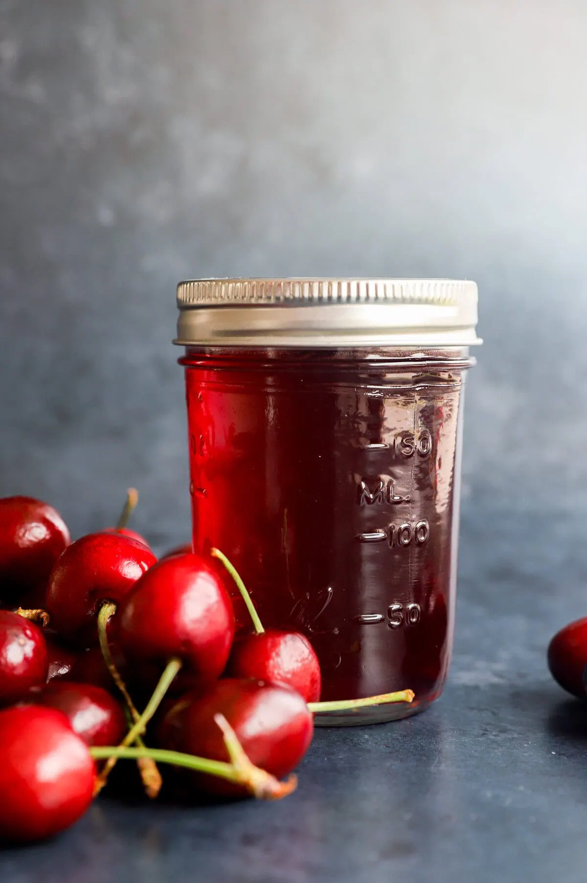 flavored syrup in a jar with fresh cherries in a pile