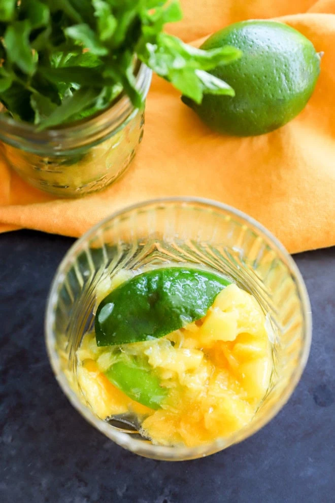 muddled mango in a glass with lime halves