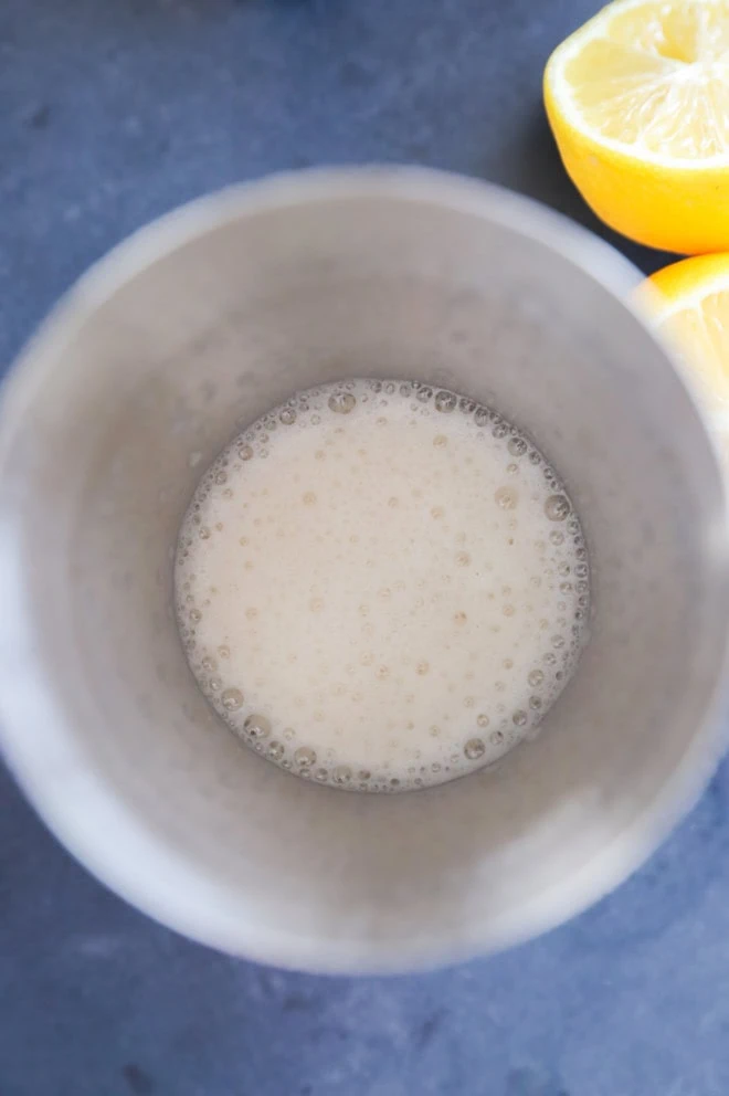 Foamy cocktail in a shaker without ice and fresh lemon halves