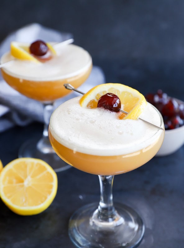 Glasses of disaronno sour cocktails with lemon and bowl of cherries