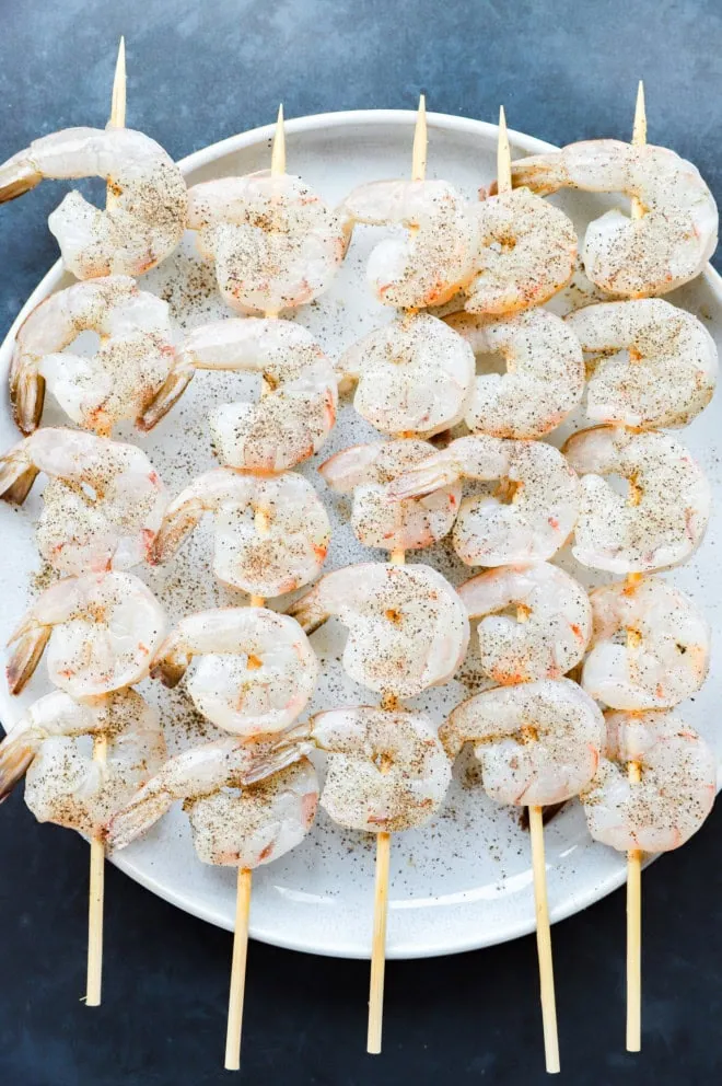Seasoned shrimp skewers on a plate before cooking