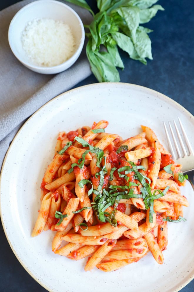 Penne pomodoro on plate with fork, fresh basil on top and grated parmesan