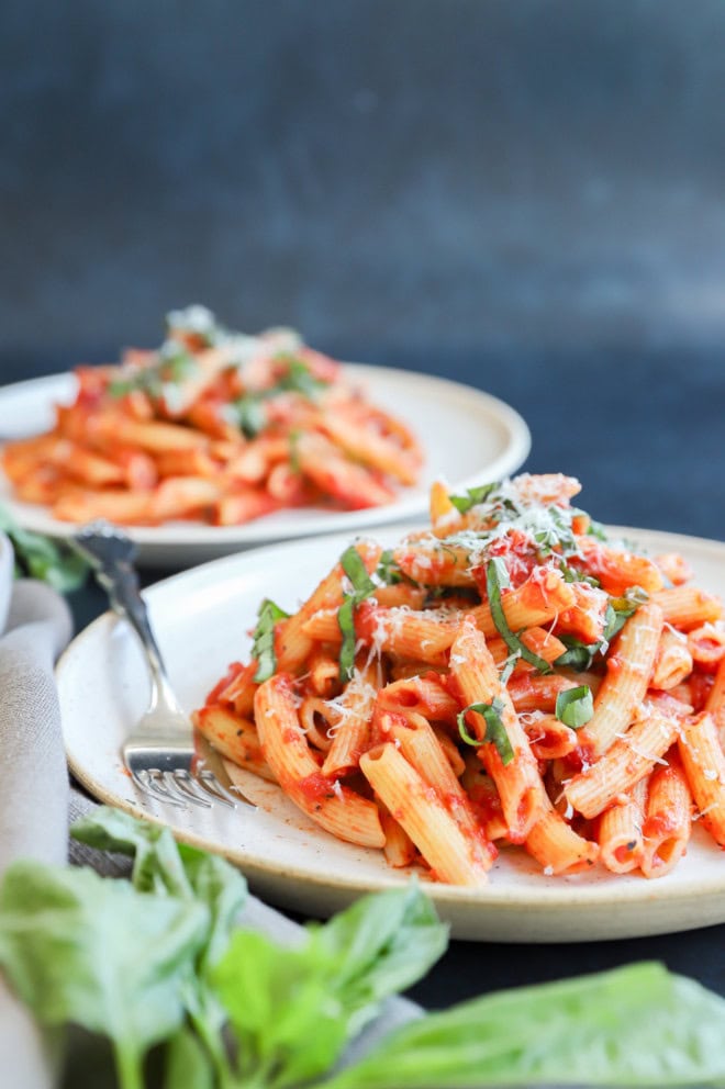 Penne pomodoro on plate with fresh basil on top and cheese