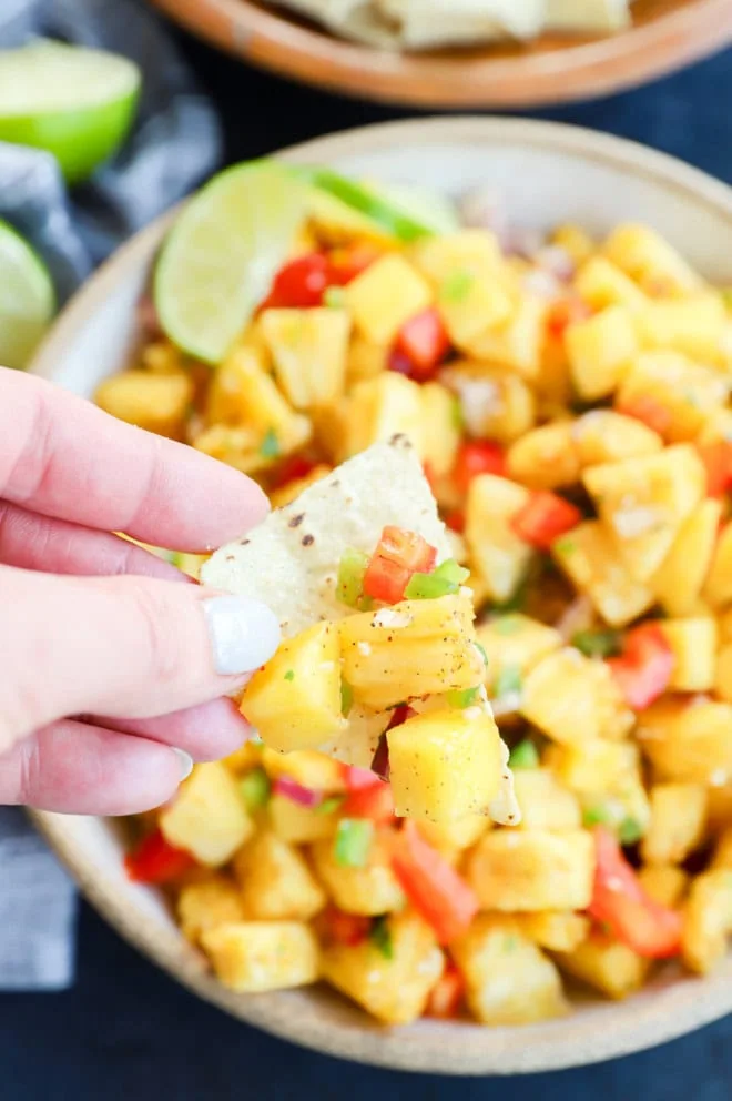 Chip with pineapple mango salsa on it and hand holding the chip
