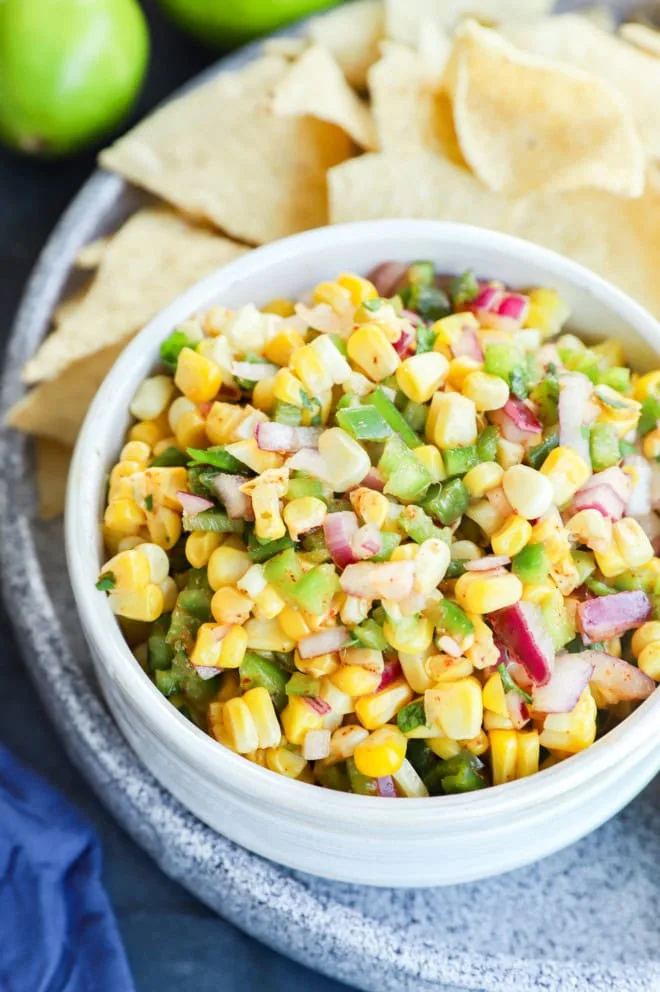 small bowl of roasted chili corn salsa with tortilla chips and limes