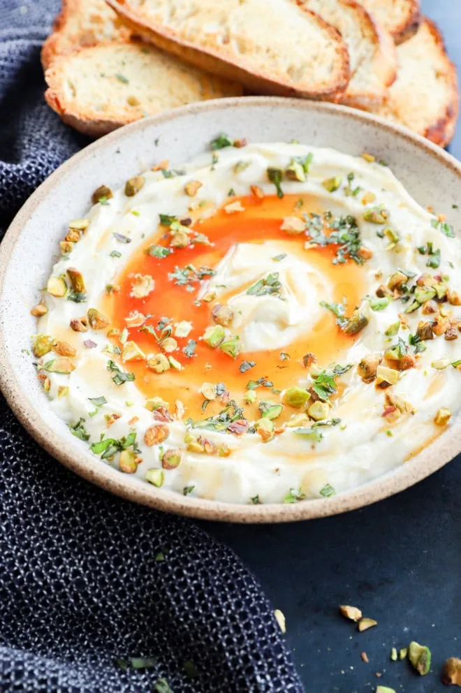 Whipped ricotta in a bowl with hot honey, nuts, and fresh herbs