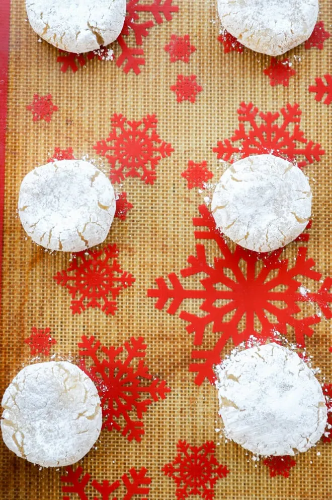 raw amaretti biscuits on lined baking sheet rolls in powdered sugar