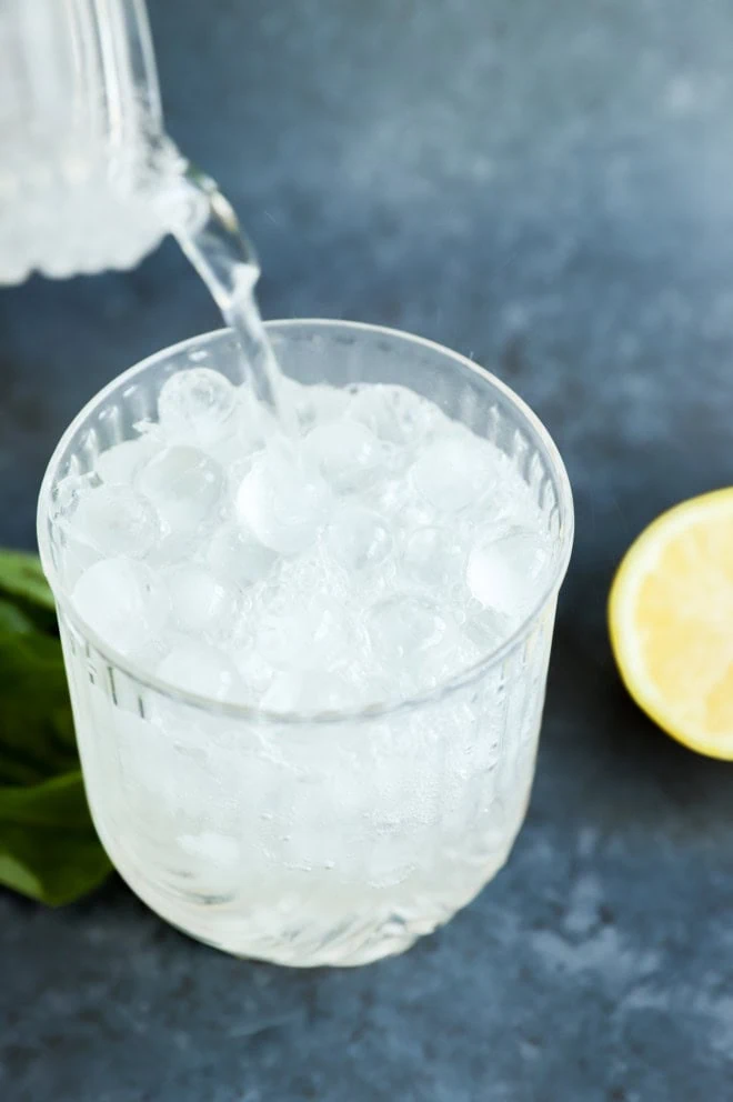 pouring soda water into a cocktail glass for gin basil smash