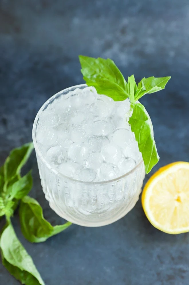 gin basil smash in cocktail with lemon half and fresh basil leaves