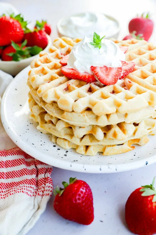 whipped cream and strawberries on top of a pile of breakfast cakes