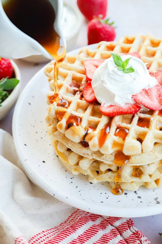 Drizzling syrup on strawberry waffles with fresh fruit and whipped cream