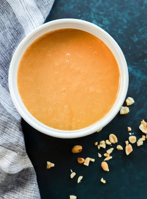 thai peanut salad dressing in a bowl with chopped peanuts around it