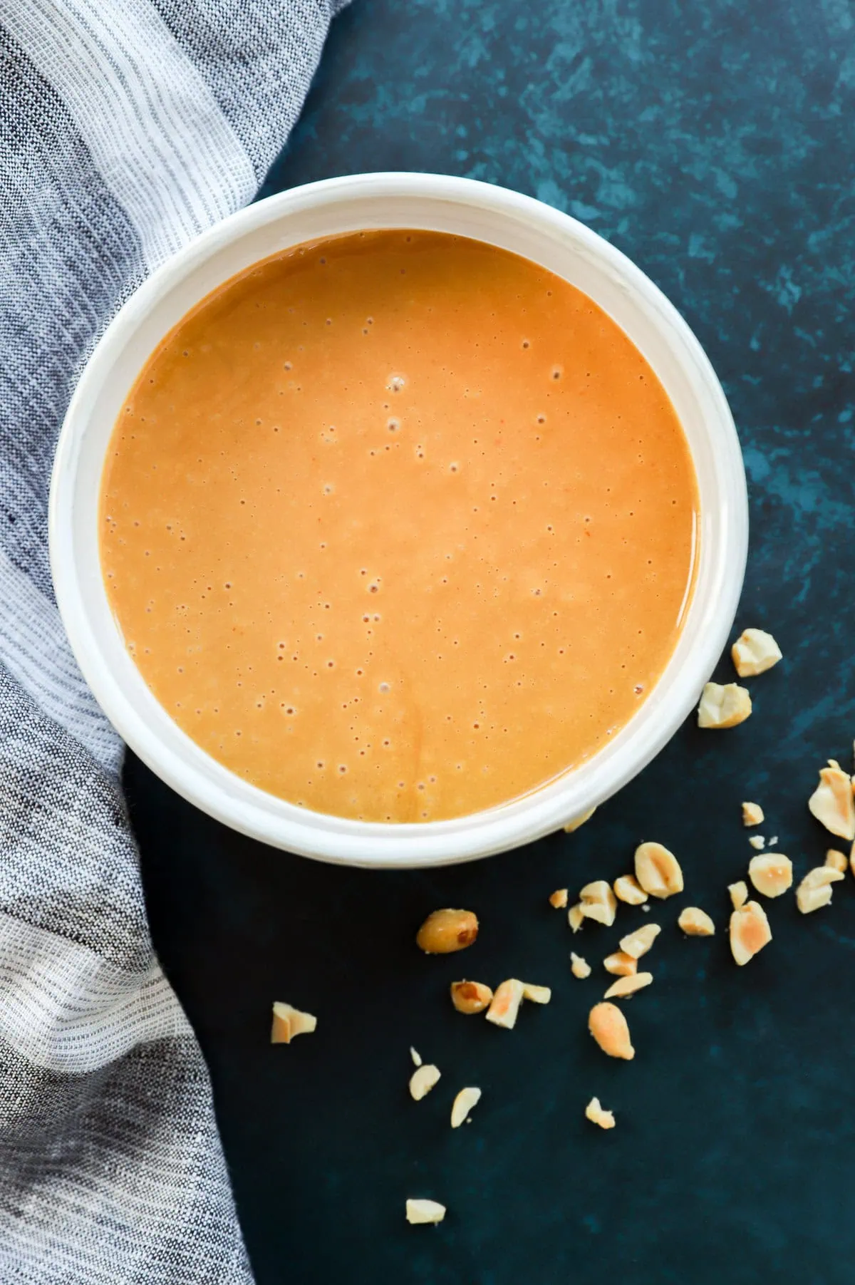 thai peanut salad dressing in a bowl with chopped peanuts around it