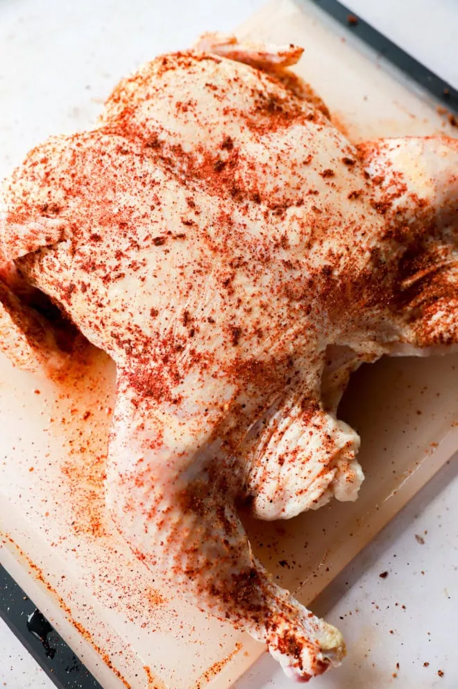 whole raw chicken with seasoning all over on cutting board