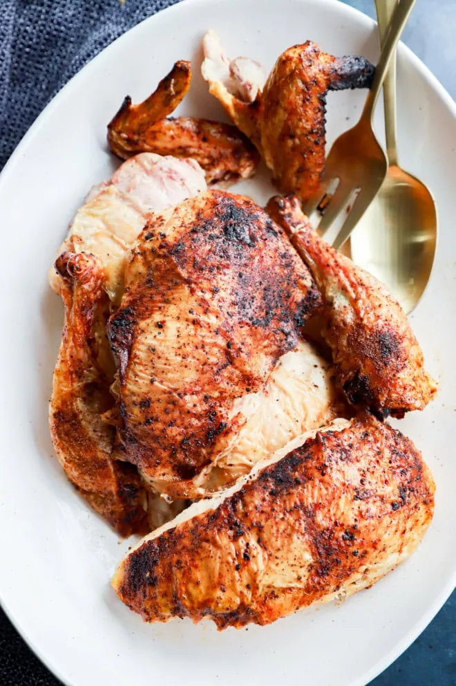 whole grilled chicken on platter in pieces with serving utensils