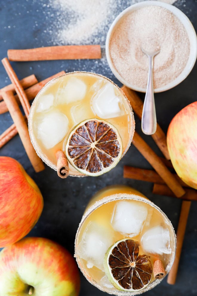 overhead image of apple cider cocktail and fresh apples and cinnamon sticks