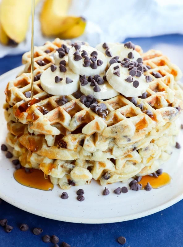 drizzling syrup on a stack of breakfast pancakes with fresh fruit and chocolate