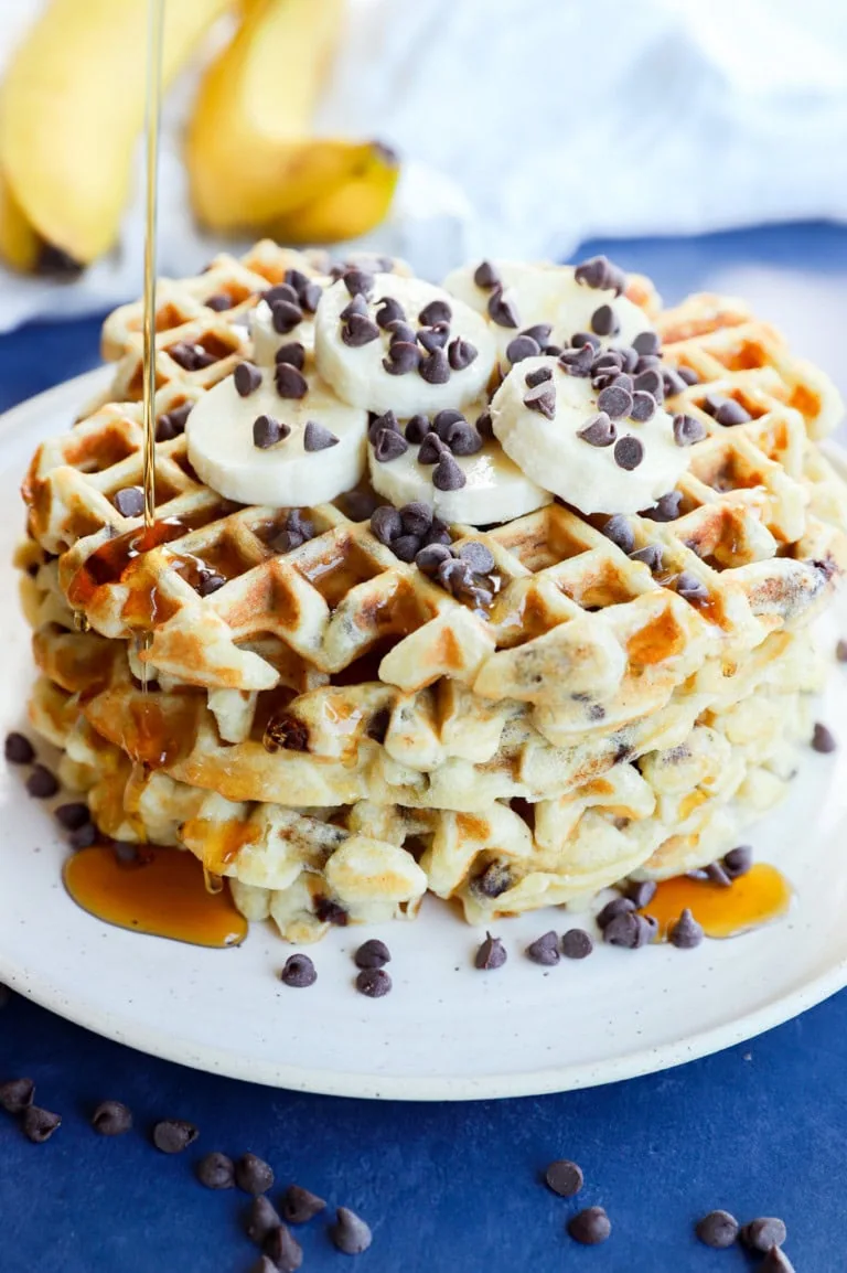 drizzling syrup on a stack of breakfast pancakes with fresh fruit and chocolate