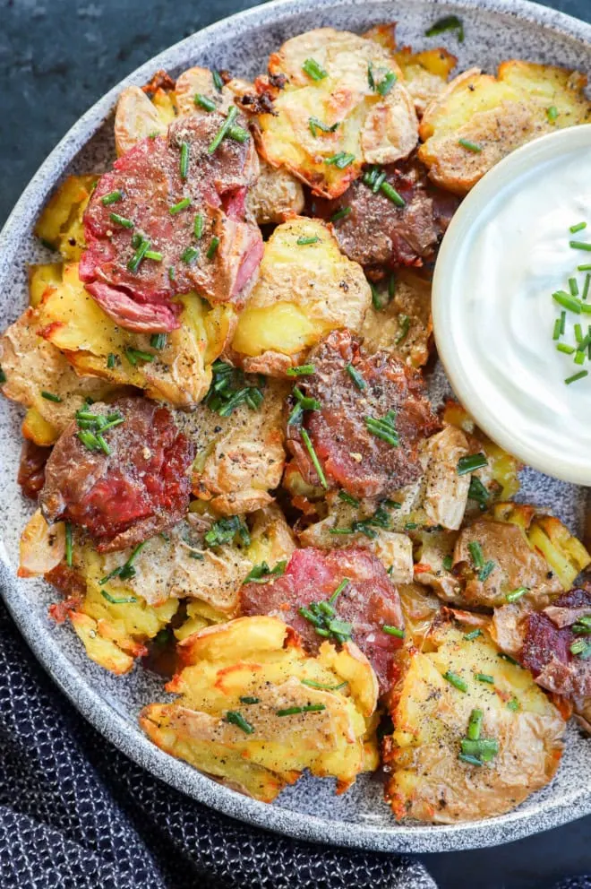 smashed fingerling potatoes on platter with sour cream in a bowl