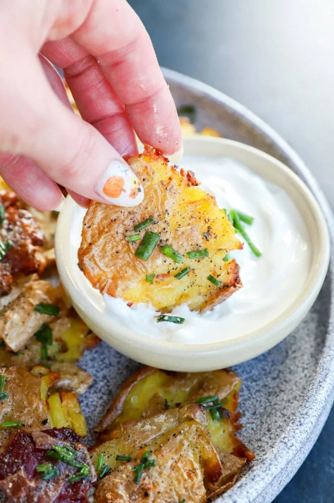 hand holding a smashed potato dipping into a bowl of sour cream