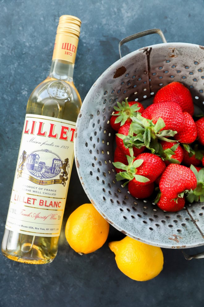 A bottle of lillet blanc, lemons, and fresh strawberries