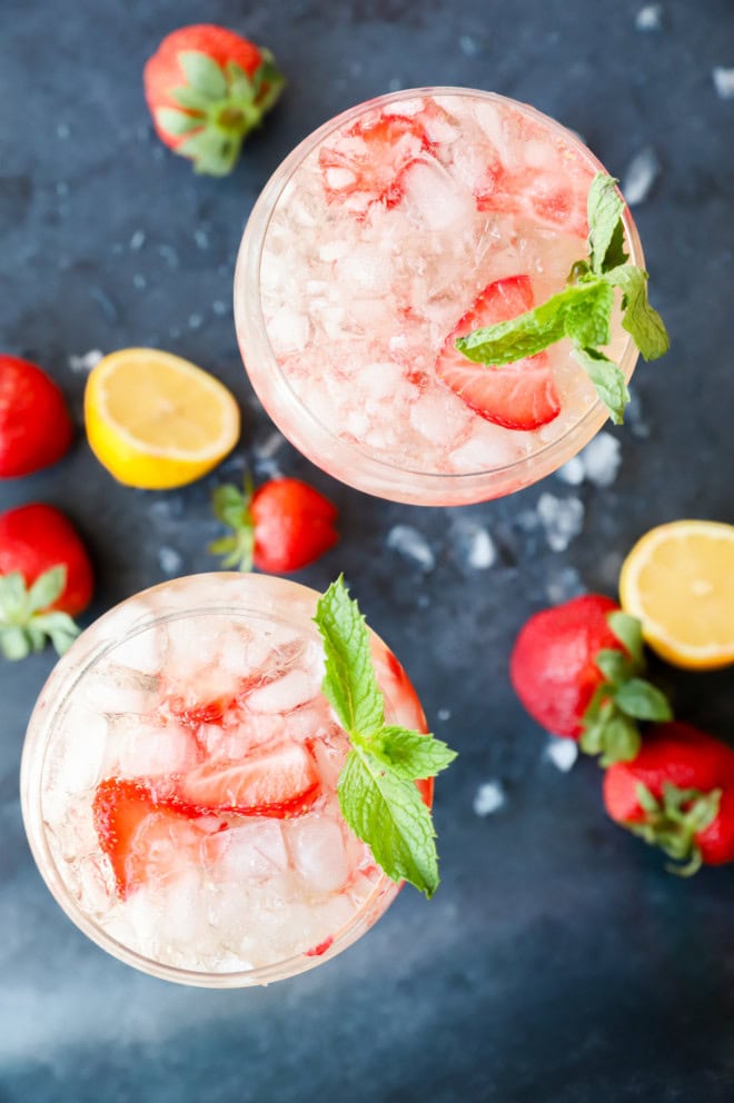 Looking down on two french cocktails in wine glasses with fresh strawberries and lemon halves