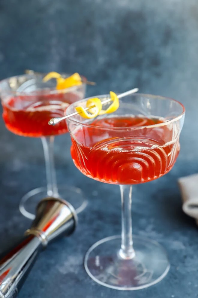 bourbon aperol drink in coupe glasses with lemon twist and jigger